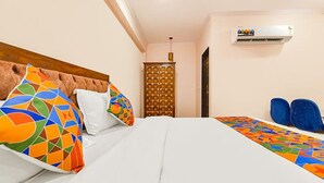 A hotel room with a bed, pillows, a headboard, a wall-mounted air conditioner, and a door. - Fabhotel Shekhawati Heritage (Jaipur)