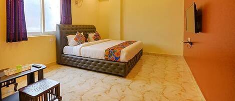 A bedroom with a bed, an air conditioner, a ceiling fan, a window, and a TV mounted on the wall.