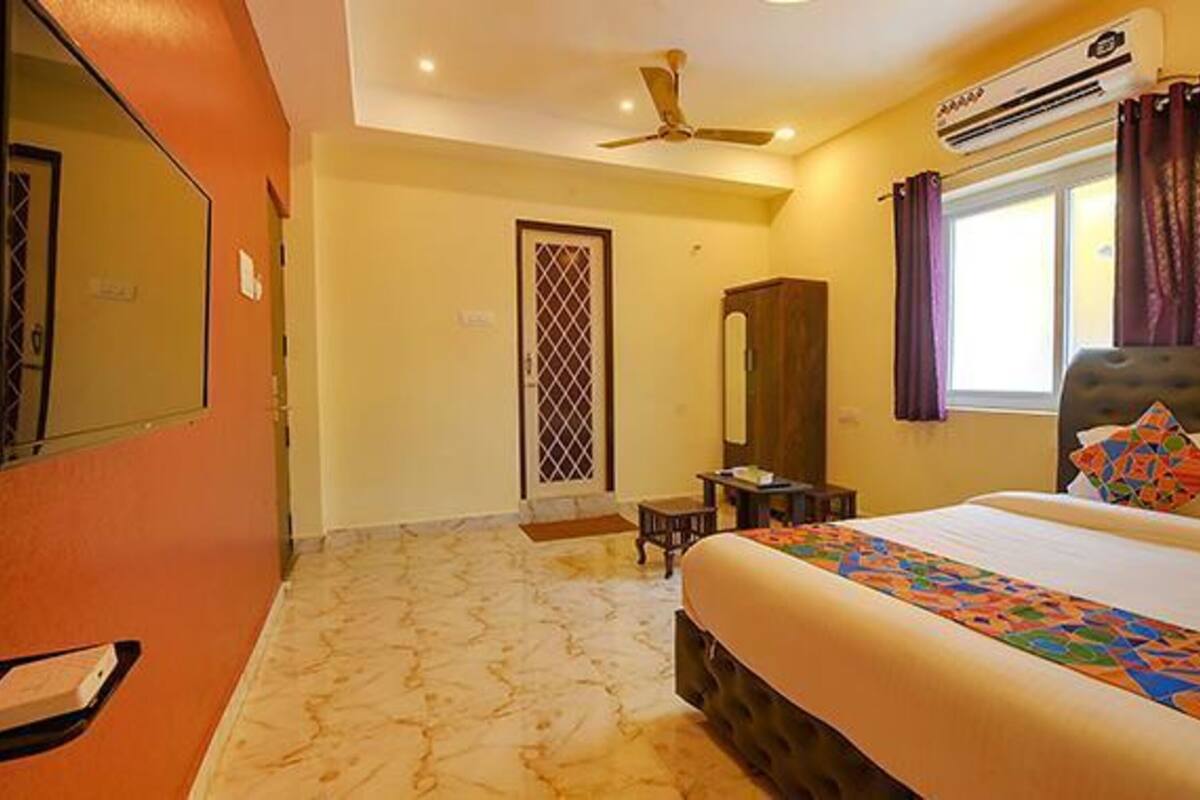 A hotel room with a bed, a wardrobe, a mirror, an air conditioning unit, and a ceiling fan.