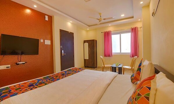 A hotel room with a bed, a desk, a chair, a television, and a window with curtains. - FabHotel The Fortune Inn - Chromepet (Chennai)