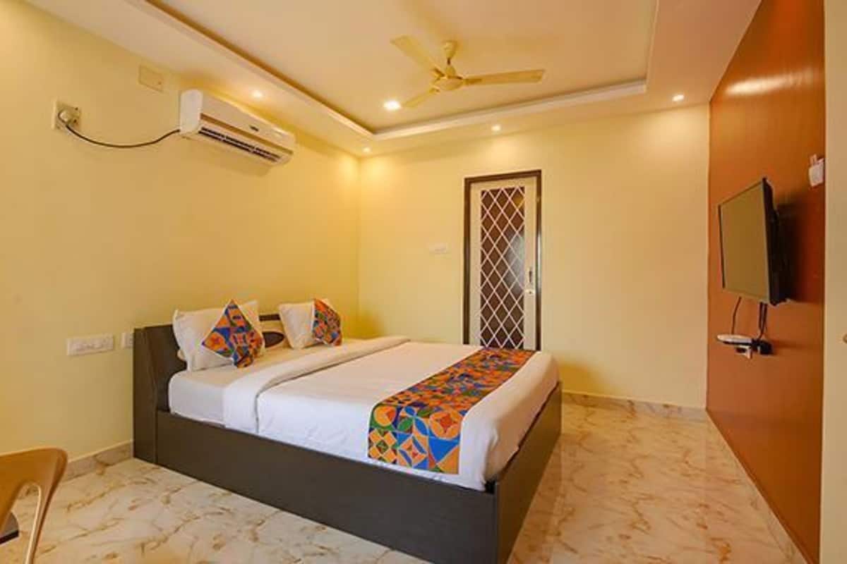 A hotel room with a bed, air conditioning unit, ceiling fan, and a television on the wall.