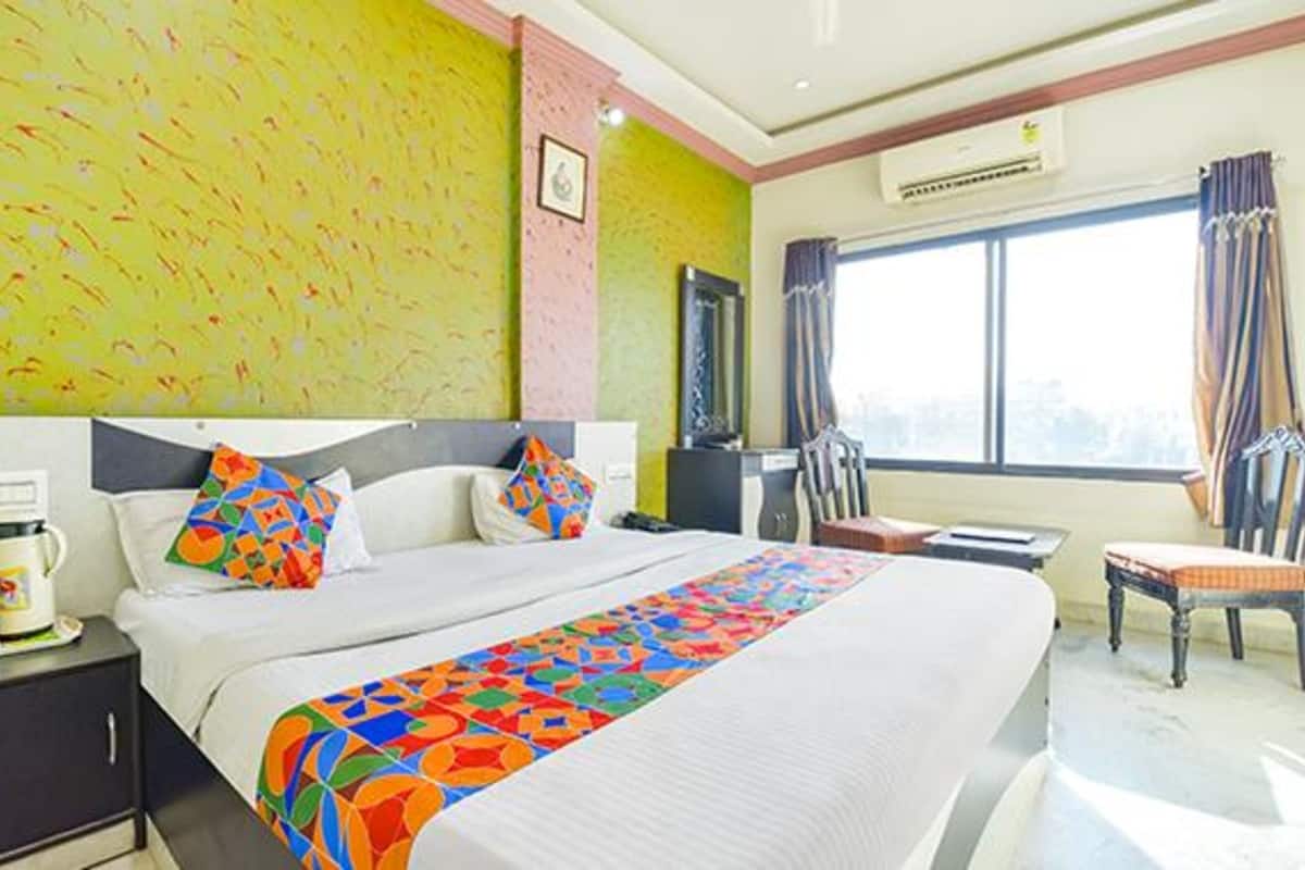 A hotel room with a large bed, a desk with a computer, a chair, and a window with curtains.