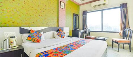 Habitación de hotel con una cama grande, un escritorio con computadora, una silla y un ventanal con cortinas.