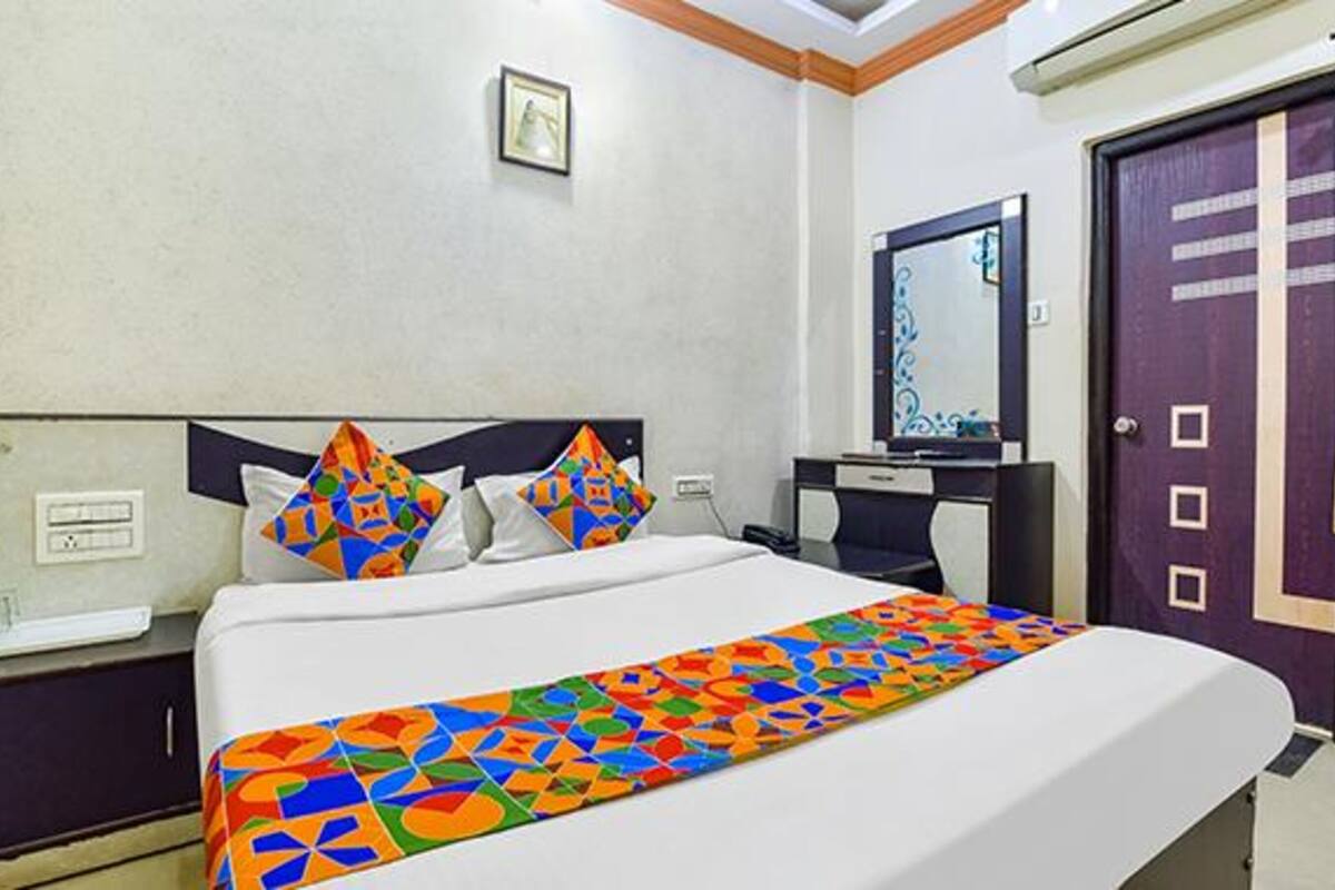 A hotel room with a bed, a nightstand, a dresser, a mirror, and a door.