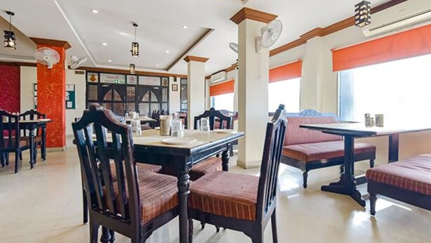 A spacious dining area with high ceilings, modern lighting, and a mix of seating arrangements including tables and booths. - Fabexpress Relax Inn I (Udaipur)