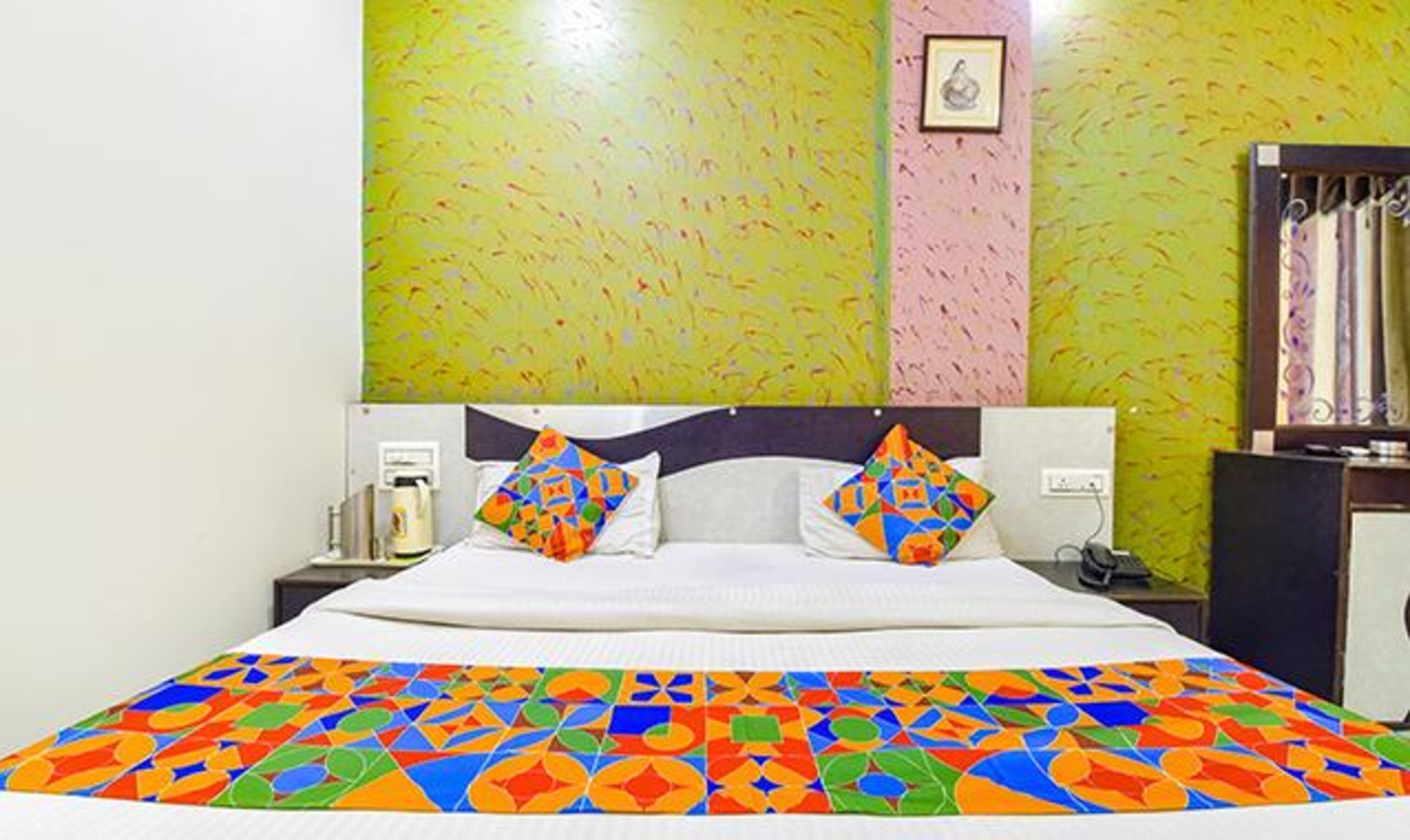 Un letto con una coperta colorata a motivi geometrici, una testiera e un comodino con una lampada.