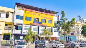 A multi-story building with a yellow facade, a sign for 'Hotel Relax Inn & Raso Restaurant', and several parked cars in front. - Fabexpress Relax Inn I (Udaipur)