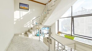 A staircase with metal railings, a view of the outside through large windows, and a picture on the wall. - Fabexpress Relax Inn I (Udaipur)