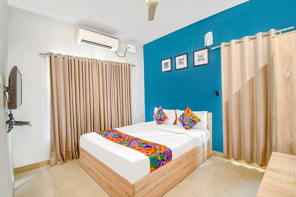 Ein Hotelzimmer mit Bett, beigen Vorhängen, einer blauen Akzentwand und einem Deckenventilator.