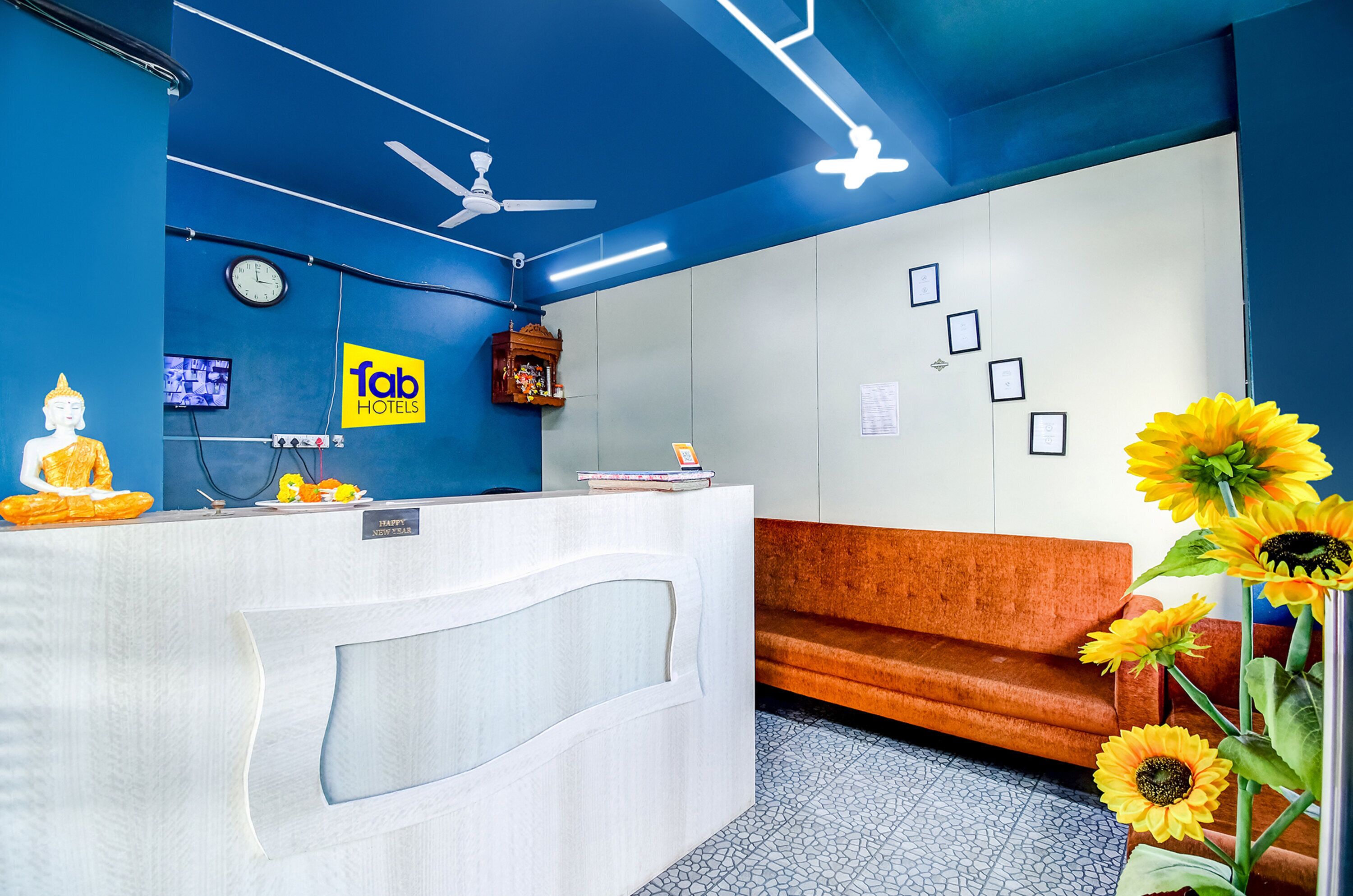 A reception area with a blue wall, a white reception desk, a clock, a ceiling fan, and a sofa.
