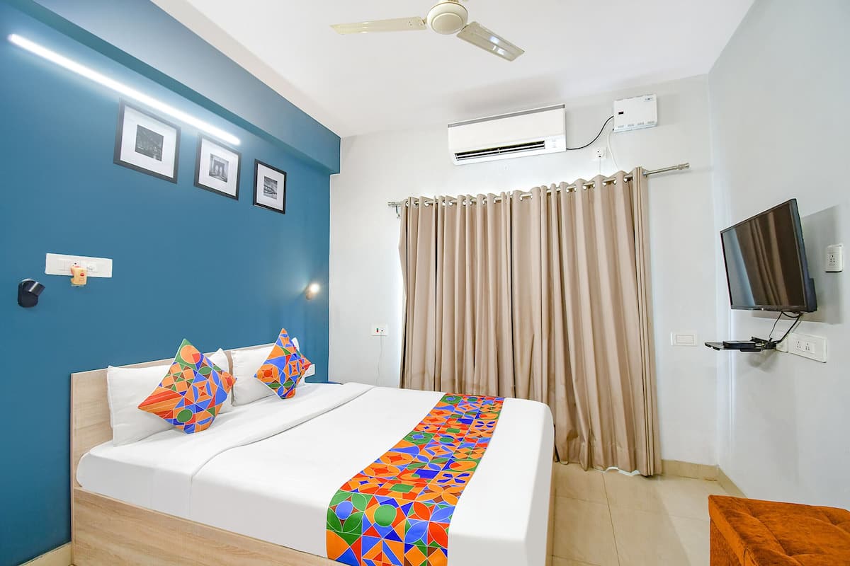 A hotel room with a bed, a ceiling fan, an air conditioning unit, a television mounted on the wall, and a window with curtains.