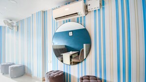 A room with striped walls, a round mirror, two ottomans, and an air conditioning unit. - Fabhotel Silverkey (Barasat)