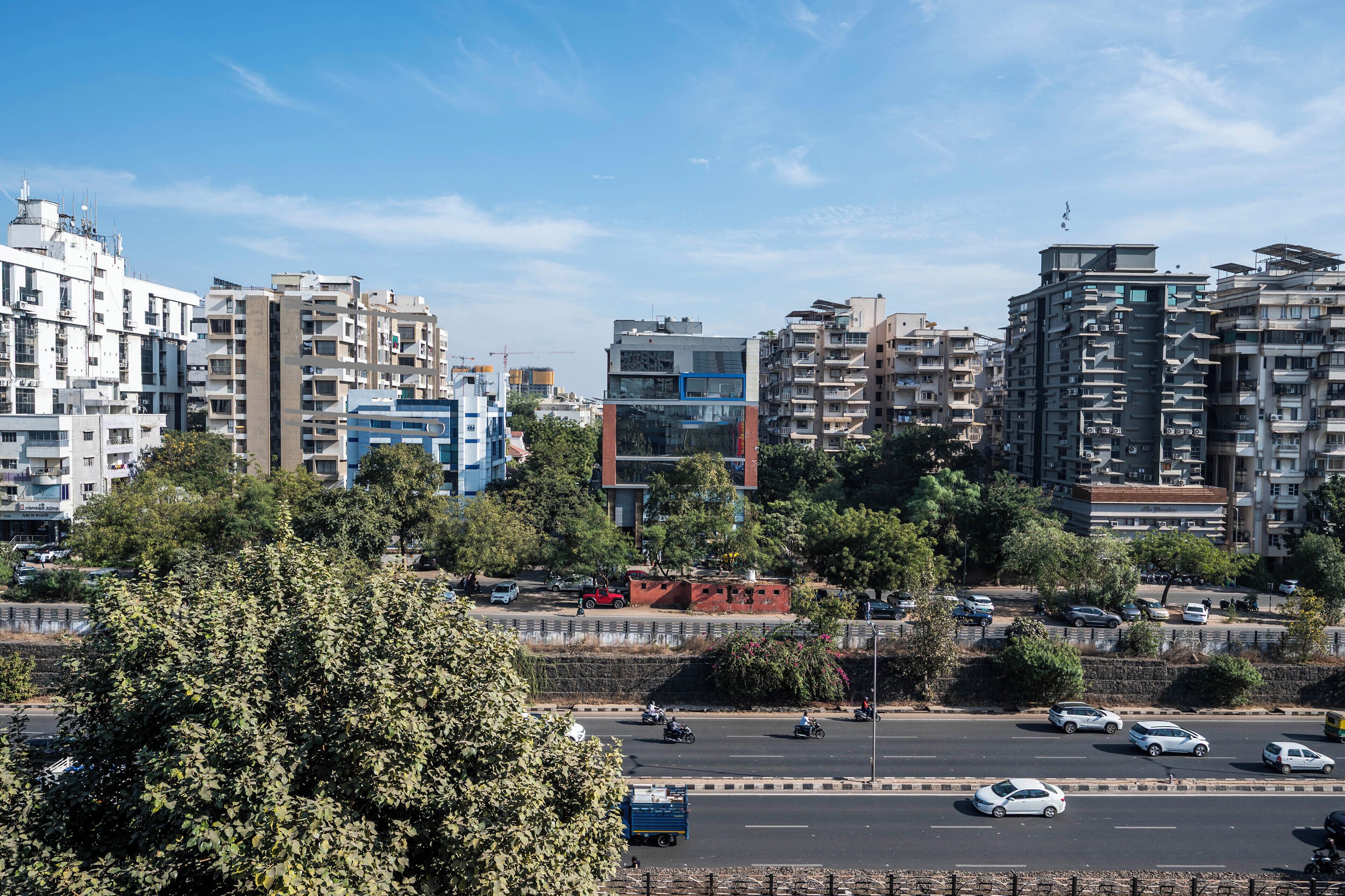 A cityscape with modern buildings, a busy road with vehicles, and trees in the foreground.