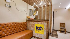 A reception area with a brown leather sofa, a reception desk with a 'fab hotels' sign, and a wooden chair. - Fabhotel New Prince Palace (Mumbai)