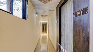 A hotel hallway with a wooden door marked "201" and a long, narrow corridor with a tiled floor. - Fabhotel New Prince Palace (Mumbai)
