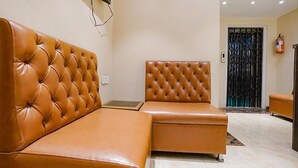 A modern living room with a brown leather sofa and ottoman, a flat-screen TV mounted on the wall, and a decorative black gate in the background. - Fabhotel New Prince Palace (Mumbai)