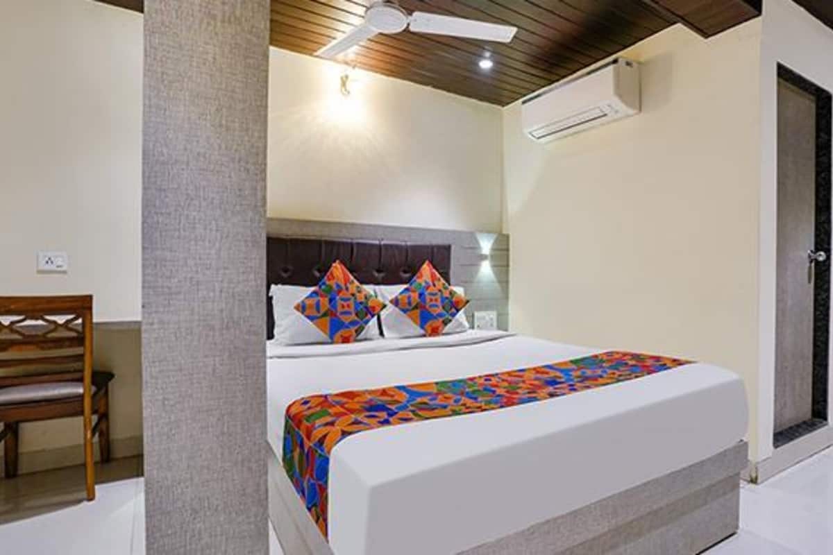 A hotel room with a bed, a chair, a ceiling fan, and an air conditioning unit.