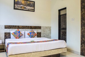 A neatly made bed with a colorful quilt, a headboard with a geometric pattern, and a framed picture of a winter landscape on the wall. - FabHotel Embassy Grand (Mumbai)