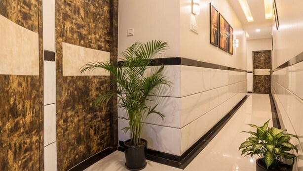 A hallway with a marble floor, a wooden door, and potted plants. - FabHotel Embassy Grand (Mumbai)
