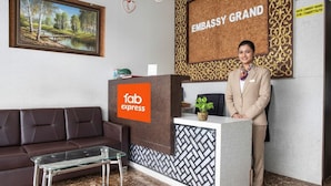 A reception area with a 'fab express' sign, a receptionist, a brown leather sofa, a glass coffee table, and a framed landscape painting. - FabHotel Embassy Grand (Mumbai)