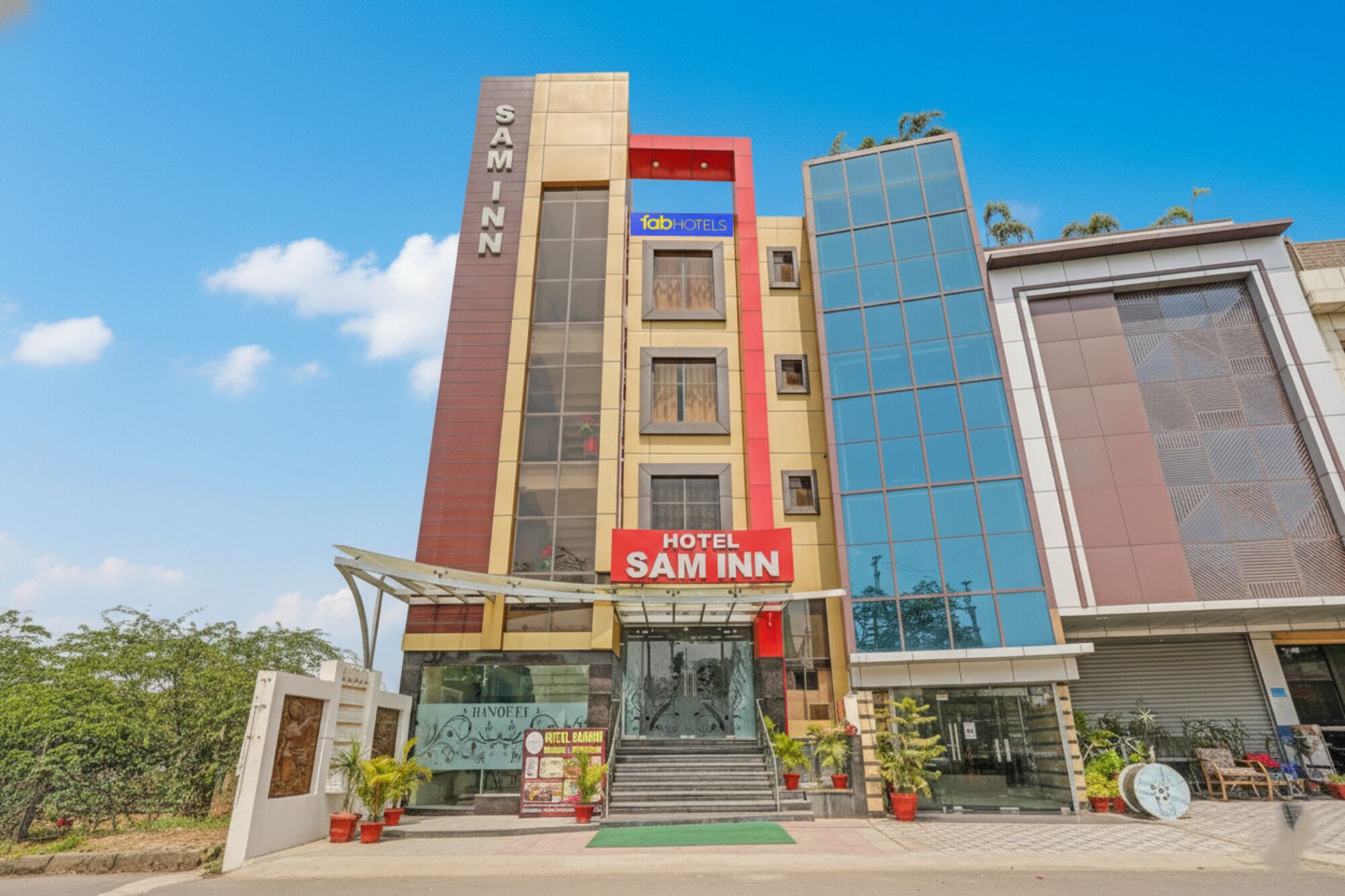 A hotel named Sam Inn with a modern facade, a prominent red sign, and a glass entrance.