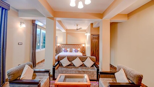 Une chambre d’hôtel avec un grand lit, un canapé et une table basse. Il y a un ventilateur de plafond et une fenêtre avec des rideaux.