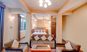 A hotel room with a large bed, a sofa, and a coffee table. There is a ceiling fan and a window with curtains.