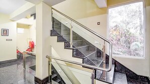 Un escalier moderne avec des rampes en verre et des marches en marbre, menant à l’étage supérieur.