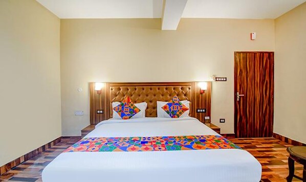 A hotel room with a large bed, a wooden headboard, and a colorful bedspread.