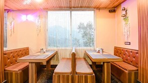 Un restaurant chaleureux avec des banquettes et des tables en bois, de grandes fenêtres ornées de rideaux et des éléments décoratifs accrochés aux murs.
