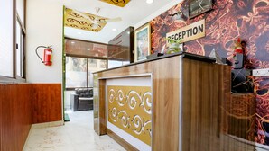 A reception area with a wooden desk, a reception sign, a fire extinguisher, and a clock on the wall. - FabHotel Limewood (Dehradun)