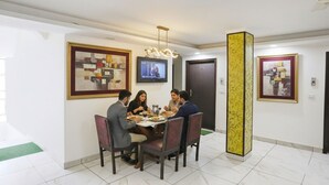 A dining area with a table set for four people, surrounded by chairs, with artwork on the walls and a television mounted above the table. - FabHotel Limewood (Dehradun)