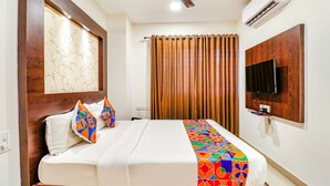Habitación de hotel con cama, ventilador de techo, aire acondicionado, televisor montado en la pared y ventana con cortinas.