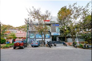 A hotel with a signboard, parked cars, and motorcycles in front. - Fabexpress Sri Sai Suites (Bengaluru)