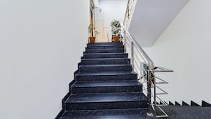 Una escalera de mármol negro con barandilla metálica, que lleva a una plataforma con plantas en macetas.
