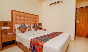A neatly made bed with a colorful geometric-patterned bedspread, a wooden headboard, and two bedside tables with lamps. - Fabexpress Emerald Inn (Mumbai)