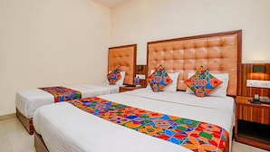 A hotel room with two beds, each with a colorful geometric-patterned bedspread. The room has a wooden headboard and a small bedside table with a lamp. - Fabexpress Emerald Inn (Mumbai)