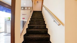 A staircase with a handrail, leading to a reception area with a counter and clocks. - Fabexpress Emerald Inn (Mumbai)