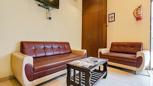 A living room with two brown leather sofas, a coffee table, and a wooden wardrobe. - Fabexpress Emerald Inn (Mumbai)