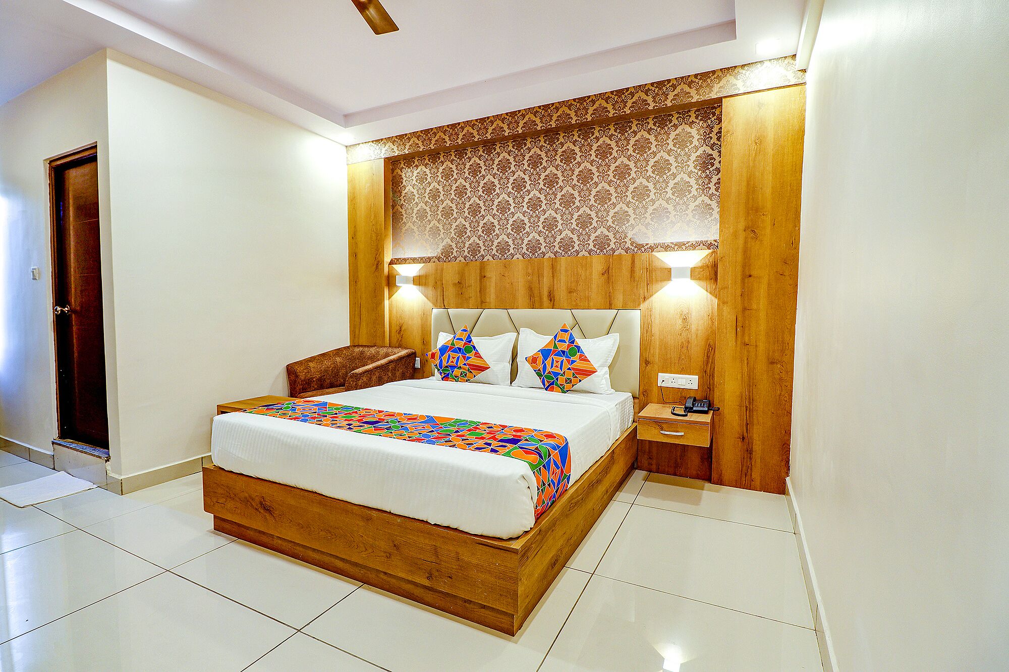 A modern bedroom with a wooden bed frame, a patterned headboard, and a bedside table with a lamp.