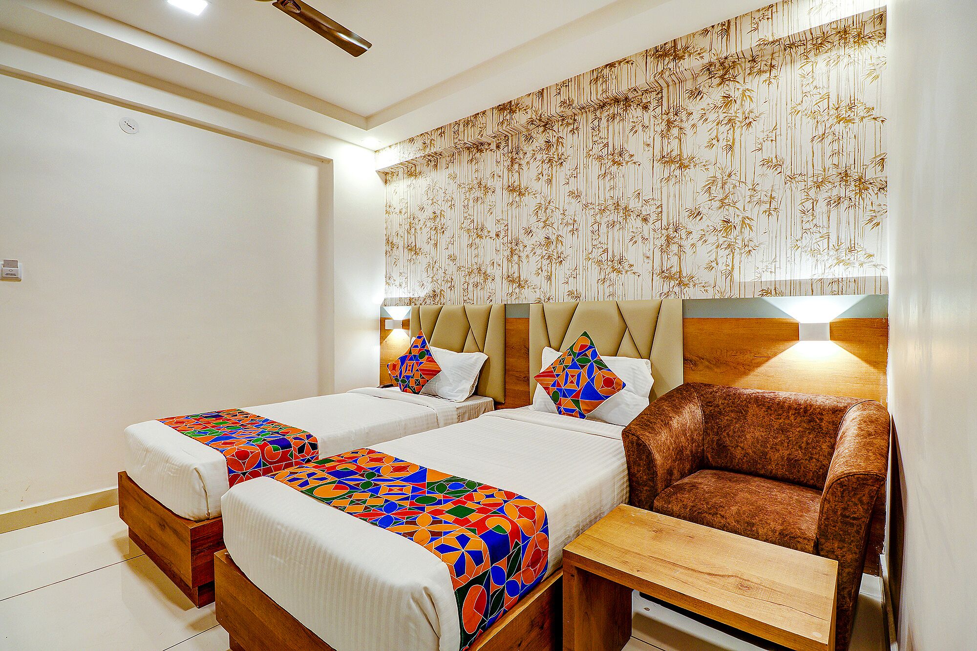 A hotel room with two beds, a brown armchair, and a wooden nightstand.