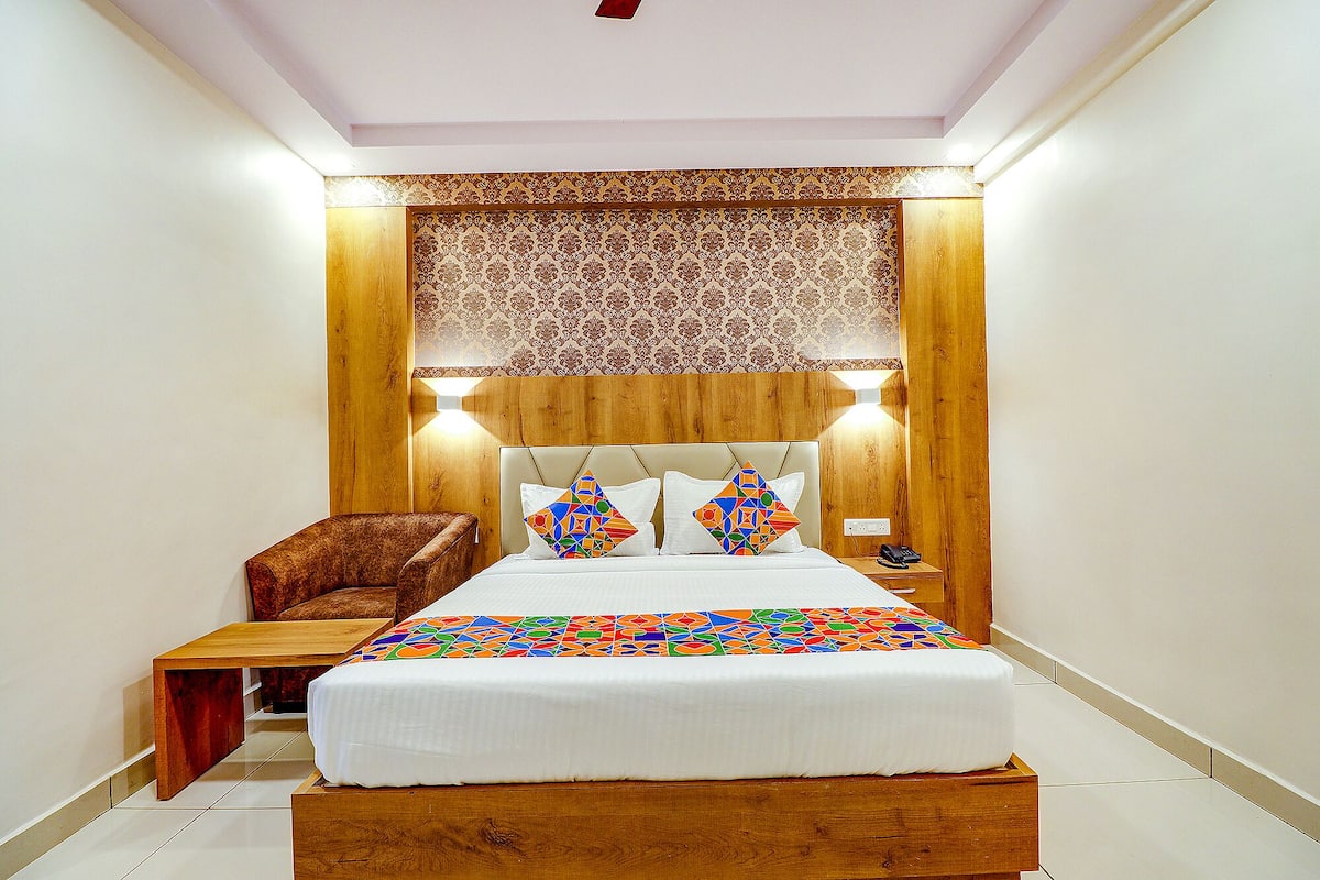 A bedroom with a wooden headboard, a bed with colorful geometric pillows, a nightstand with a phone, and a wooden bench.