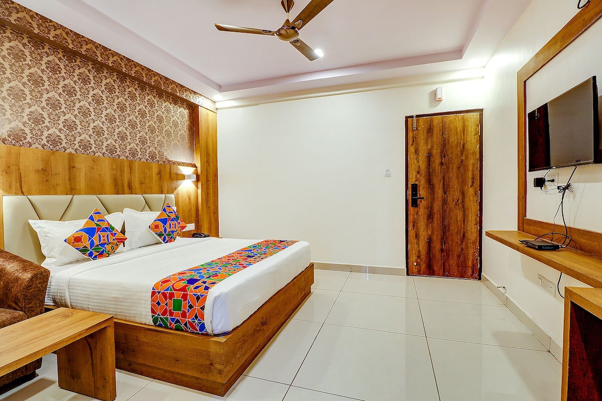 A hotel room with a bed, bedside table, wooden headboard, and a television on a wooden stand.