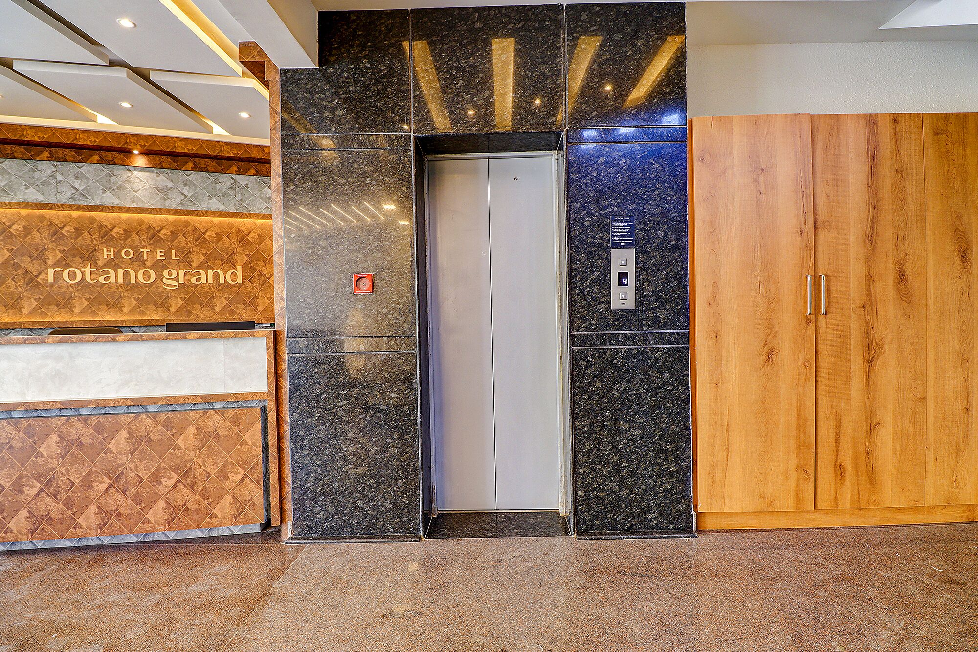 Una entrada de hotel con un muro de mármol, un ascensor y una puerta de madera.