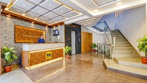 A hotel reception area with a modern design, a reception desk, a TV screen, and a staircase leading to upper floors. - FabHotel Rotano Grand Marathahalli (Bengaluru)