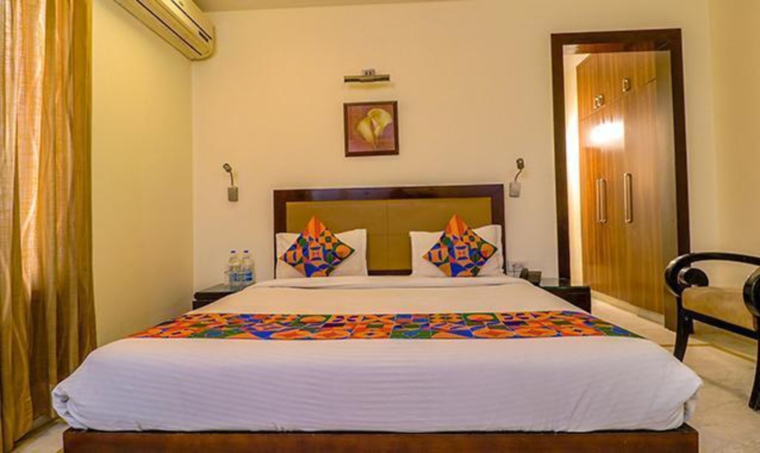 A hotel room with a bed, a chair, a wardrobe, and a painting on the wall.