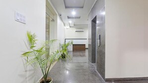 A modern hallway with a reception desk, potted plants, and a polished floor. - FabHotel The Gahmar Inn (Lucknow)