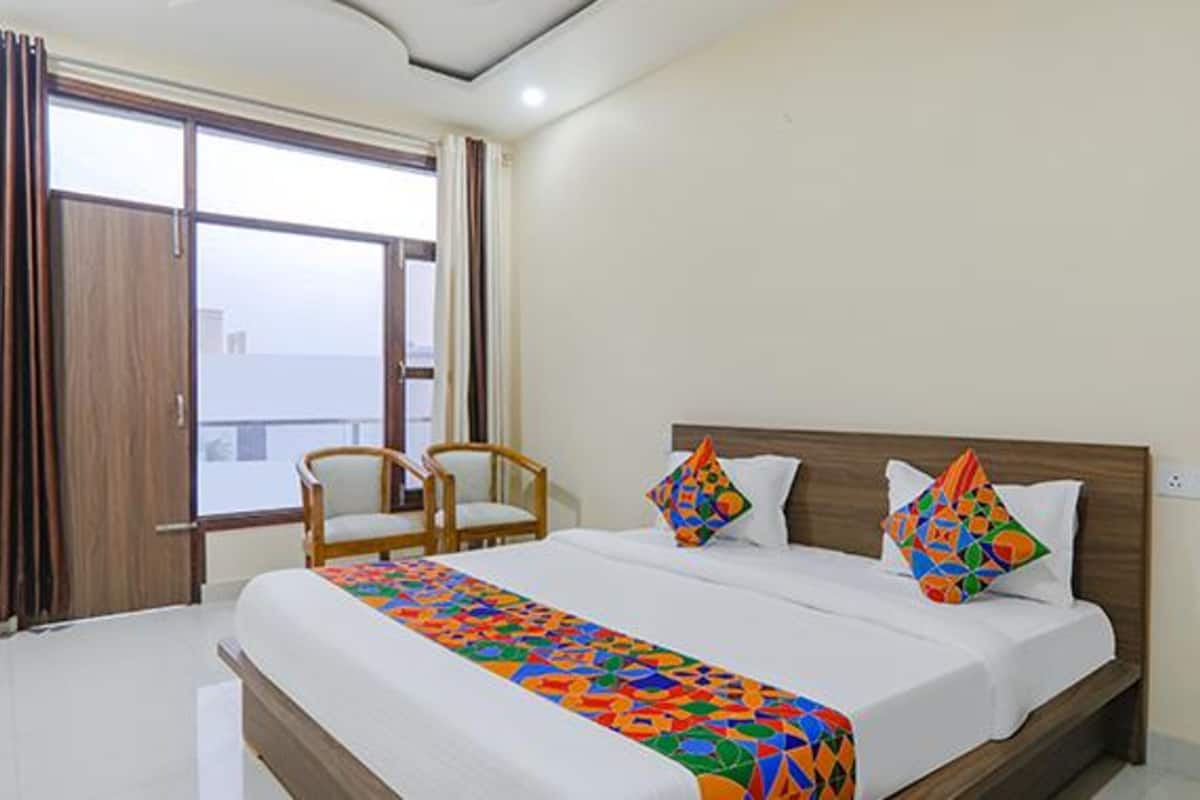 A hotel room with a large bed, two chairs, a window with curtains, and a view of the city.