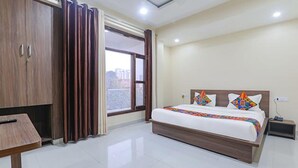 A hotel room with a large bed, a wooden wardrobe, a desk, and a window with curtains. - FabHotel The Gahmar Inn (Lucknow)