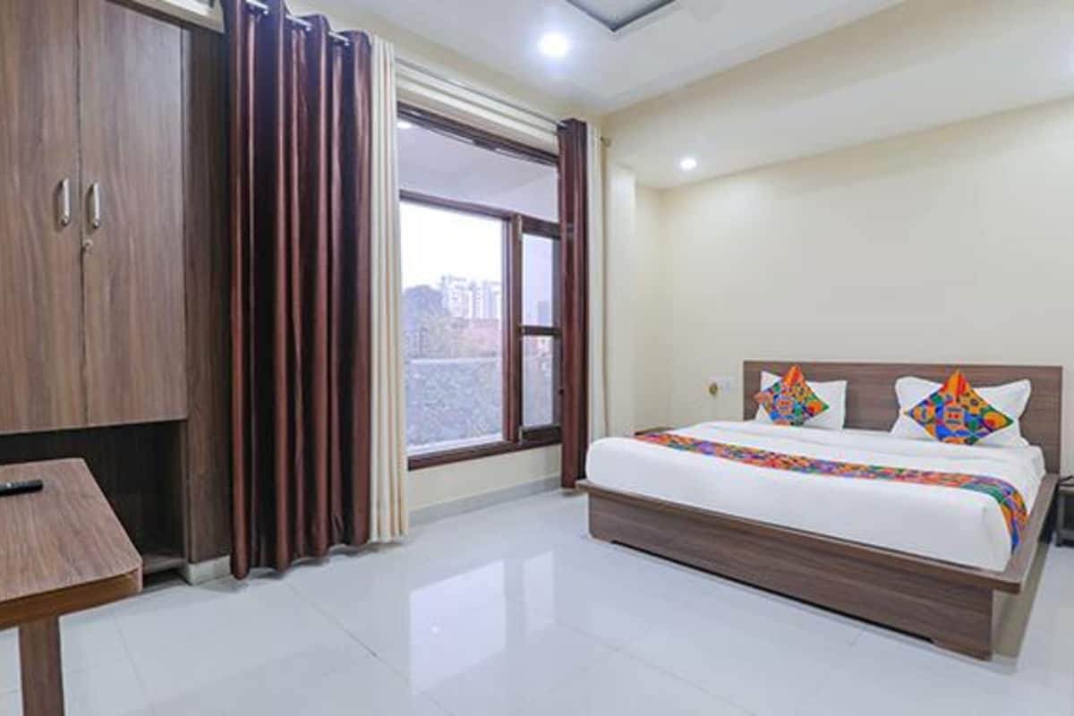 A hotel room with a large bed, a wooden wardrobe, a desk, and a window with curtains.